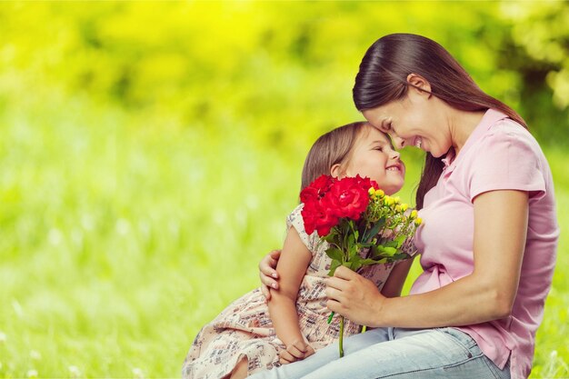 Mère et fille avec bouquet de fleurs sur fond flou vert.