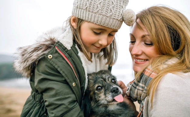 Mère et fille caressant leur chien sur la plage en hiver