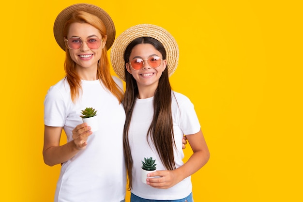 Mère et fille en chapeau de paille et lunettes de soleil avec plante en pot sur fond jaune