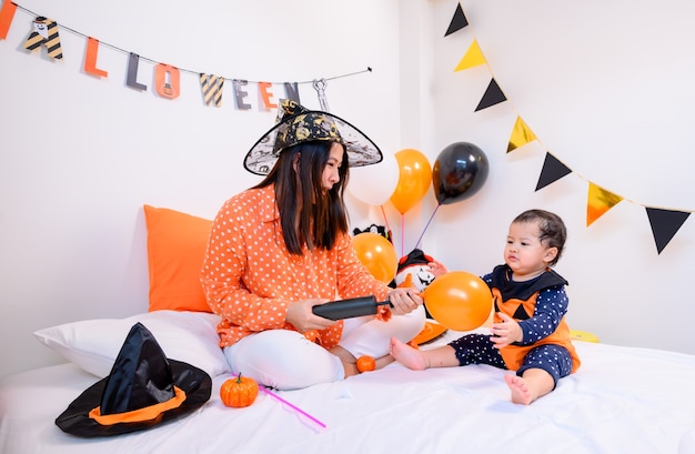 Mère avec fille en costume pour célébrer Halloween à la maison. Kid avec maman dans la décoration de la chambre.