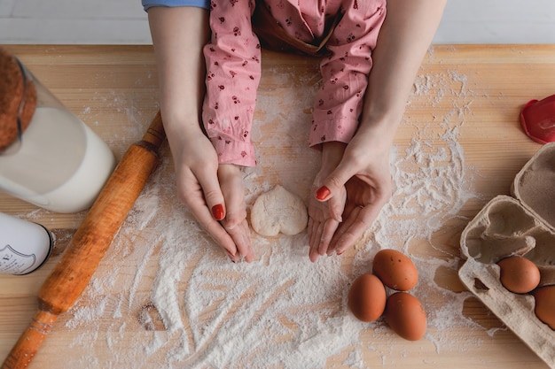 mère et fille dans la cuisine préparent des aliments à partir de farine et dessiner des cœurs sur la farine