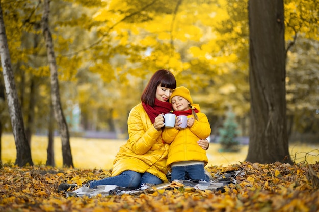 Mère et fille dans le parc jaune d'automne, buvant du thé chaud