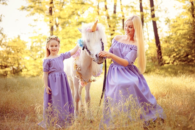 Photo mère et fille dans des robes lavande similaires caressent un cheval licorne. prairie d'été