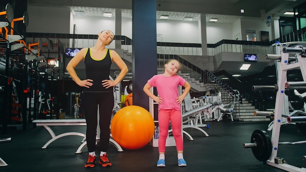 Mère et fille dans la salle de sport La famille effectue des exercices physiques Fitness Mode de vie sain Concept d'entraînement familial sportif heureux Femme avec son enfant faisant des étirements d'échauffement dans la salle de sport