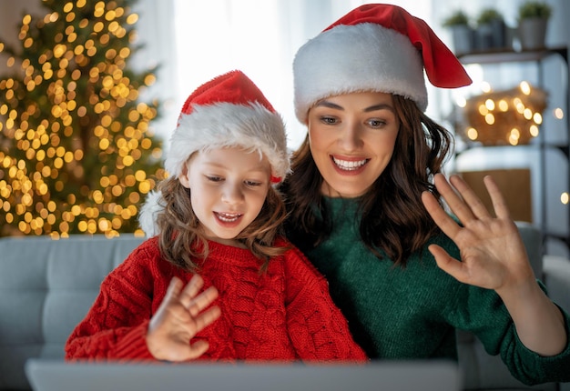 Mère et fille discutent avec quelqu'un utilisant un ordinateur portable dans le salon décoré pour Noël.