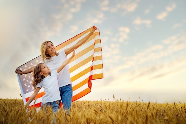 Photo mère et fille avec drapeau américain dans un beau champ de blé