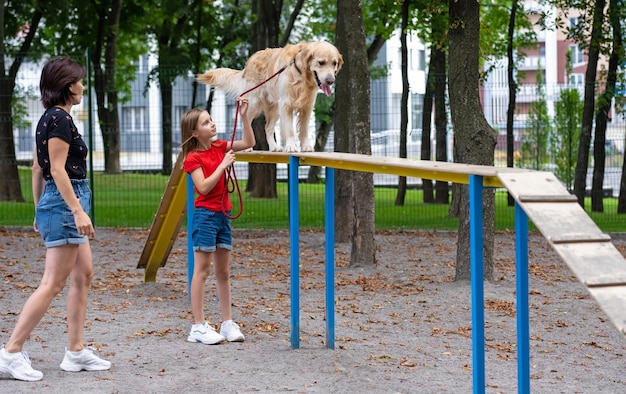 Mère avec fille dressant un chien golden retriever dans le parc à la famille des filles d'été avec un toutou pe...