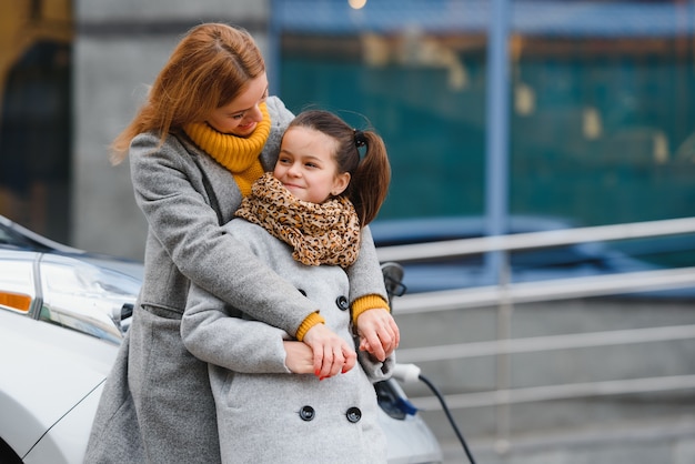 Une mère et une fille élégantes chargent une voiture électrique et passent du temps ensemble