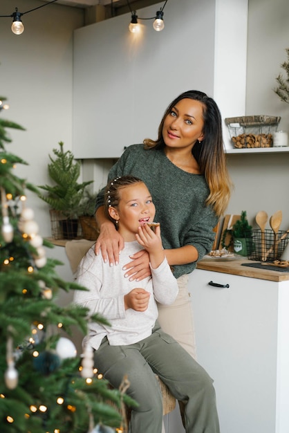 Une mère et une fille élégantes en vêtements faits maison mangent des biscuits de Noël dans la cuisine