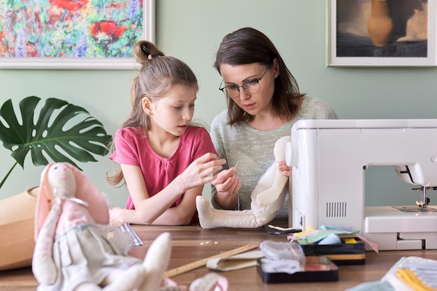 Mère et fille enfant cousant ensemble lièvre jouet, passe-temps et loisirs à la maison. Famille, vie, créativité, parent enseignant les compétences des enfants, fête des mères