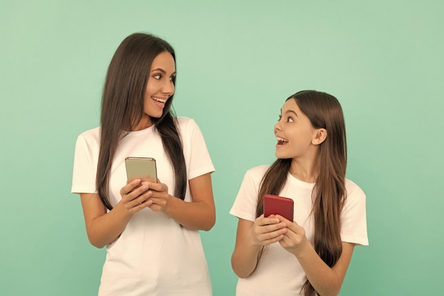 Mère et fille étonnées discutant sur smartphone sur fond bleu