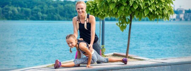 Mère et fille faisant des exercices de gym sur l'herbe à l'embarcadère de la rivière