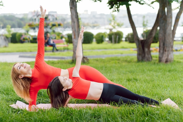 Mère et fille faisant des exercices de yoga sur l'herbe dans le parc à la journée