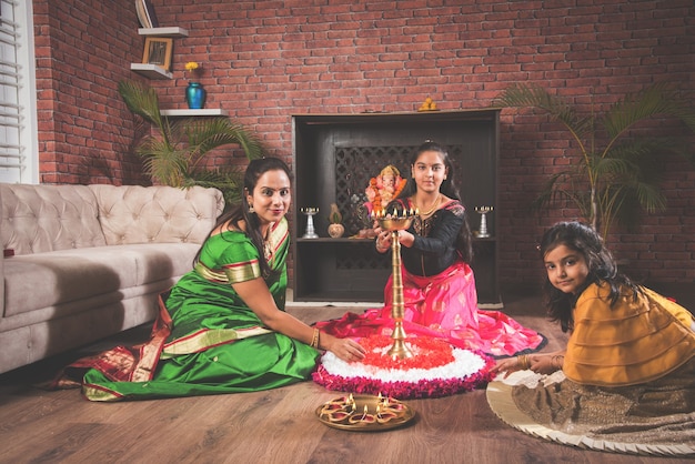 Mère et fille faisant des fleurs rangoli et fille allumant diya ou samai