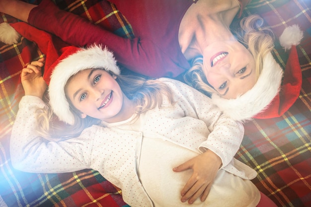 Mère et fille festive souriant à la caméra sur une couverture à la maison dans le salon