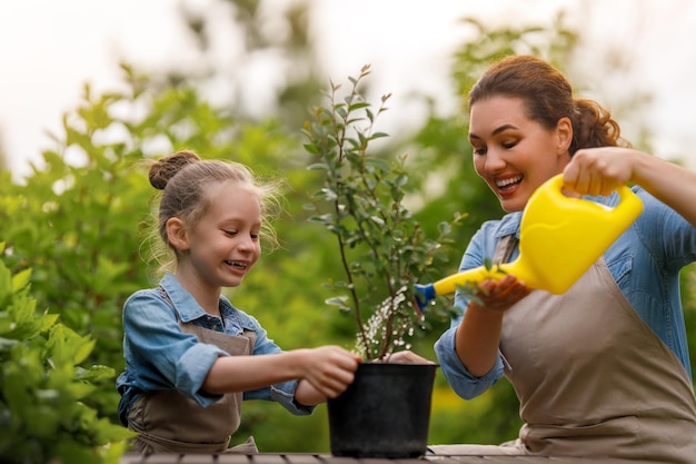 Mère et fille heureuses au jardin, enfant aidant sa mère et apprenant la botanique.