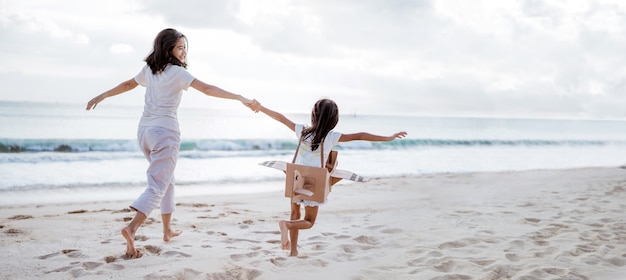 Mère et fille jouant avec un avion en carton sur la plage ensemble