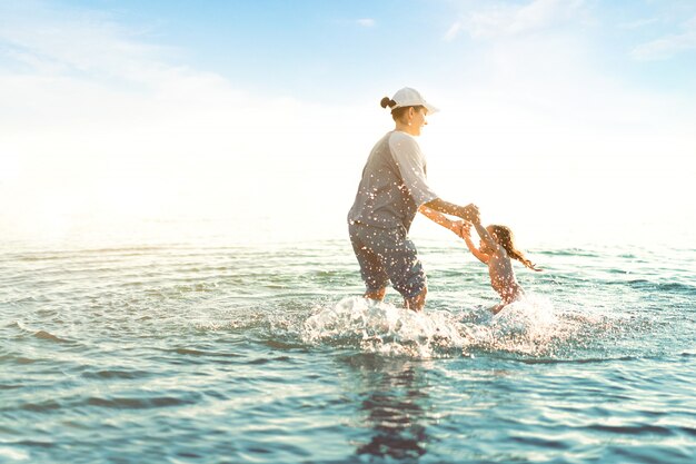 Mère Et Fille Jouant à La Mer. Loisirs D'été Actifs Pendant Les Vacances. Maman Et Enfant S'amusant Sur L'eau. Tenant Ses Enfants Sur Les Mains Et La Tordant.