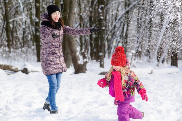 Mère et fille jouent des boules de neige dans la forêt d'hiver