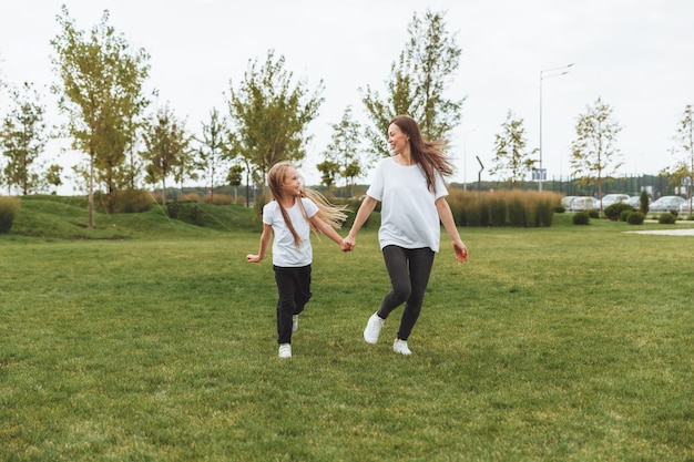 Mère et fille jouent et courent autour du parc par une belle journée la famille s'amuse dans le parc sur l'herbe du jogging matinal