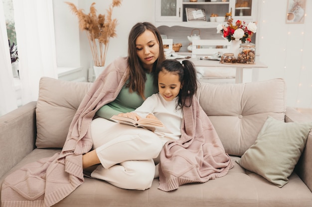 Mère et fille lisent un livre sur le canapé du salon. concept d'enseignement à domicile.