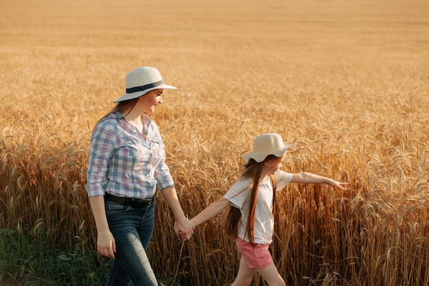 Mère et fille marchent près du champ de blé doré, une famille d'agriculteurs heureux, femme et enfant avec ha...