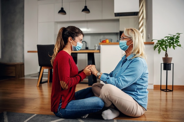 Mère et fille avec des masques chirurgicaux protecteurs assis sur le sol et se tenant la main pendant l'épidémie de virus corona. Même s'il s'agit d'une épidémie corona, nous pouvons toujours partager l'amour.