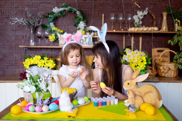 La mère et la fille de Pâques peignent des œufs de Pâques avec un sourire de peinture et se préparent pour les vacances à la maison dans la cuisine dans les oreilles d'un lièvre