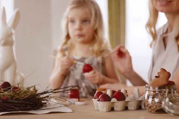 Mère et fille peignent des oeufs de Pâques dans la chambre à la table de vacances.