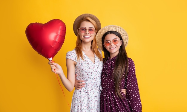 Mère et fille positives tiennent un ballon coeur d'amour sur fond jaune