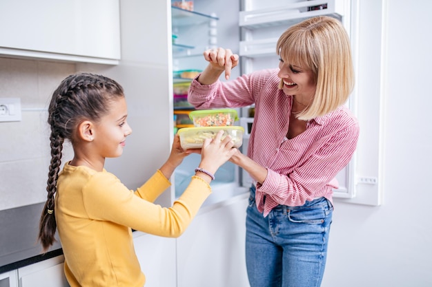 Mère et fille préparant ensemble des légumes pour l'hiver dans des récipients sous vide.