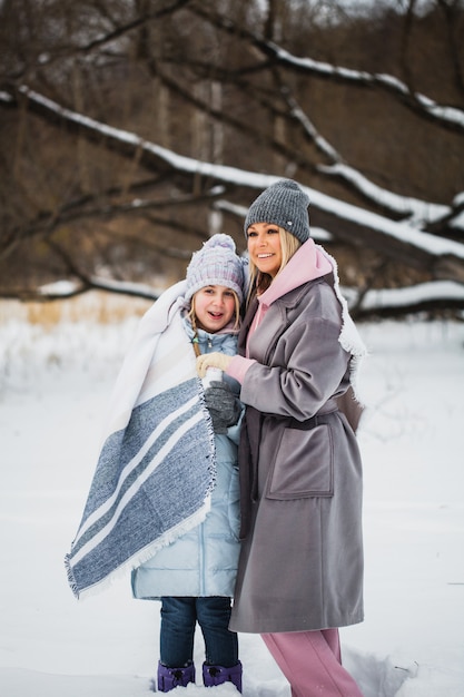 Photo mère et fille sur une promenade d'hiver, enveloppée dans une couverture, forêt, champ, hiver