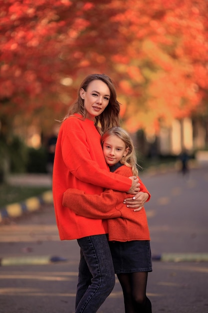 Mère et fille en pulls orange s'amusent lors d'une promenade dans la rue près des maisons de campagne