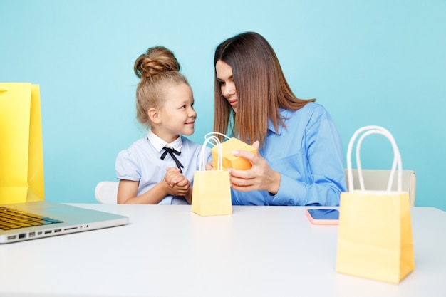 Mère et fille regardant des cadeaux assis à la table blanche dans la salle bleue.