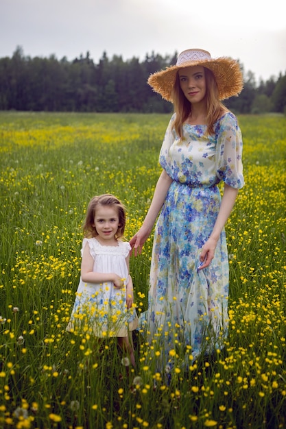 Mère et fille en robes et un chapeau se tiennent dans un champ de fleurs jaunes dans la journée d'été