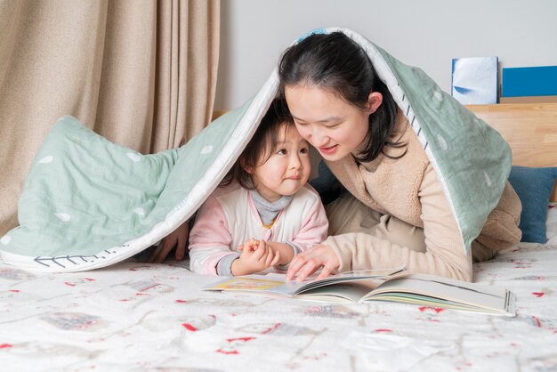 Mère et fille s'asseoir sur le lit lisant ensemble