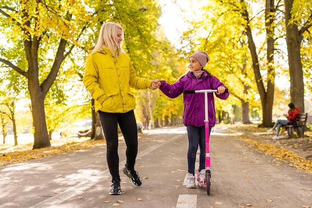 Mère et fille se promènent à l'automne dans le parc. La petite fille monte un scooter