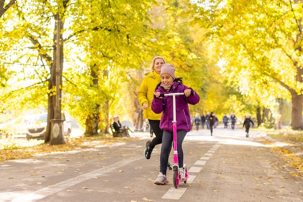 Mère et fille se promènent à l'automne dans le parc. La petite fille monte un scooter