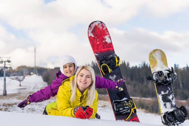 mère et fille avec des snowboards dans une station de montagne