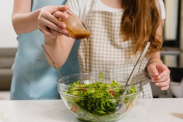 Mère et fille ou sœurs préparant un repas sain - salade fraîche avec tomates et légumes verts, ajoutez une sauce mélangée avec de l'huile et du jus de citron dans un petit bol. Fermer.