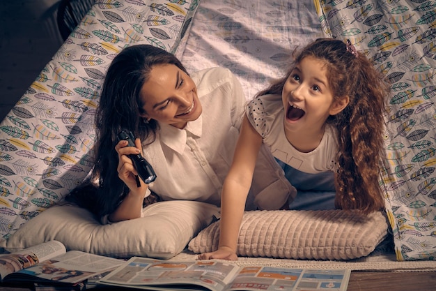 La mère et la fille sont assises dans une tente tipi, lisant des histoires avec la lampe de poche. Famille heureuse.