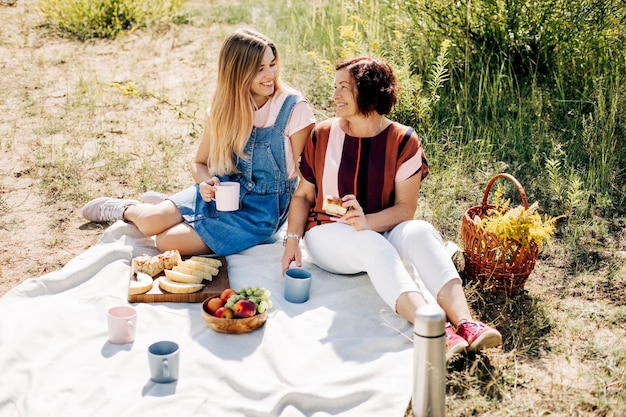 Photo une mère et une fille souriantes font un pique-nique avec des fruits et des pâtisseries sur la pelouse.