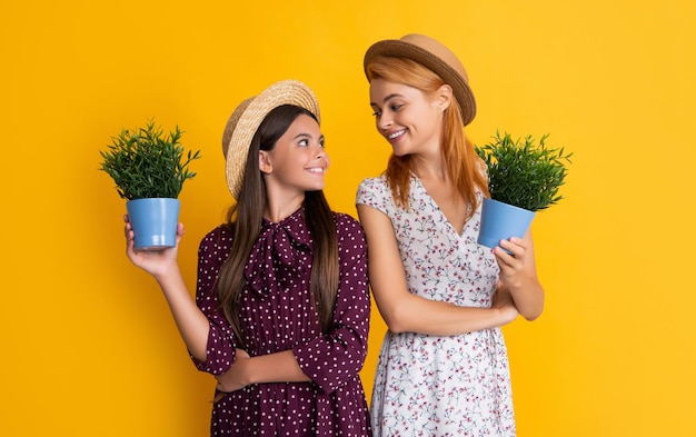 Mère et fille sourient avec une plante en pot sur fond jaune