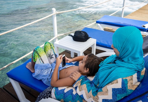 Mère et fils arabes assis et profitant de la jetée de la plage