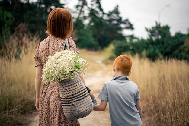 Mère et fils aux cheveux rouges avec un grand bouquet de fleurs sauvages dans la nature en été