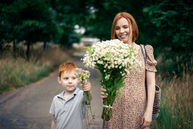 Mère et fils aux cheveux rouges avec un grand bouquet de fleurs sauvages dans la nature en été