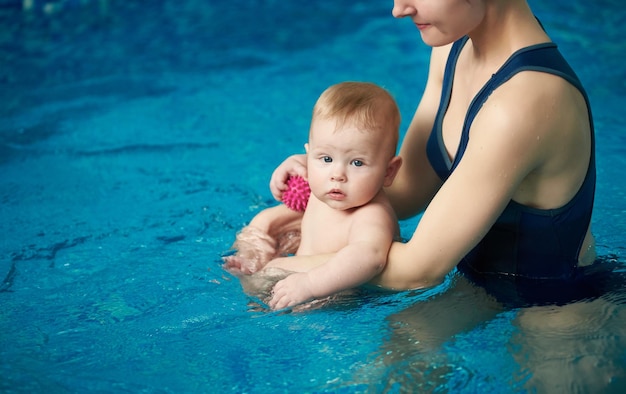 Photo mère et fils dans la piscine doux bébé assis dans les bras de la mère pendant l'exercice pour le développement de l'enfant dans l'eau