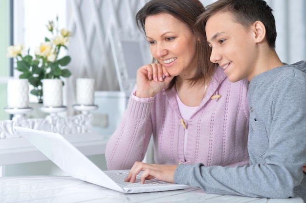 Mère et fils émotionnels utilisant un ordinateur portable moderne et posant à la maison