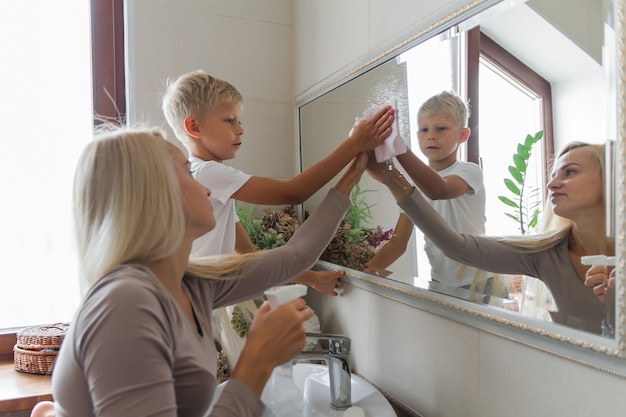 La mère et le fils font le ménage ensemble et nettoient le miroir de la salle de bain