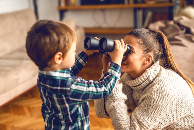 Mère et fils jouant dans l'appartement. Enfant mettant des jumelles aux yeux de la femme.